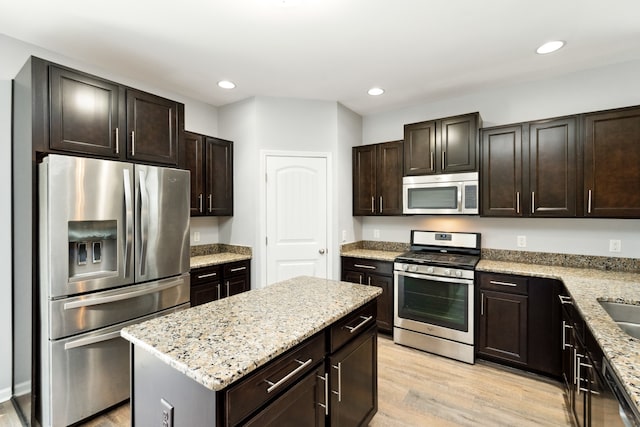 kitchen with light stone counters, dark brown cabinets, stainless steel appliances, light hardwood / wood-style floors, and a kitchen island