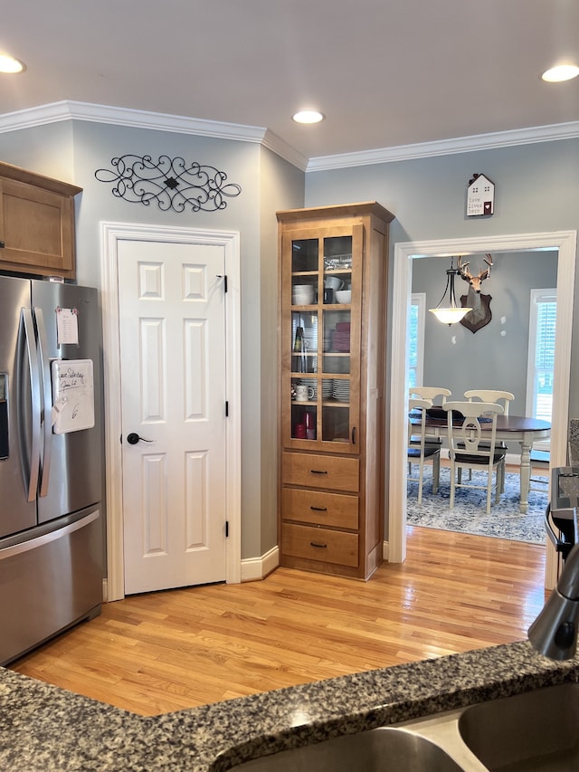 kitchen featuring stainless steel refrigerator with ice dispenser, light wood-type flooring, ornamental molding, and dark stone countertops