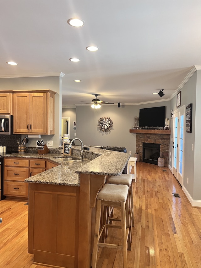 kitchen with stone counters, sink, crown molding, and light hardwood / wood-style flooring