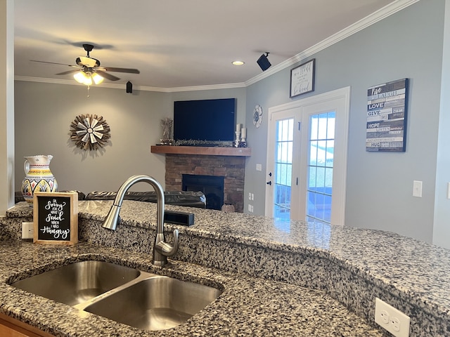 kitchen featuring ceiling fan, a stone fireplace, ornamental molding, and sink