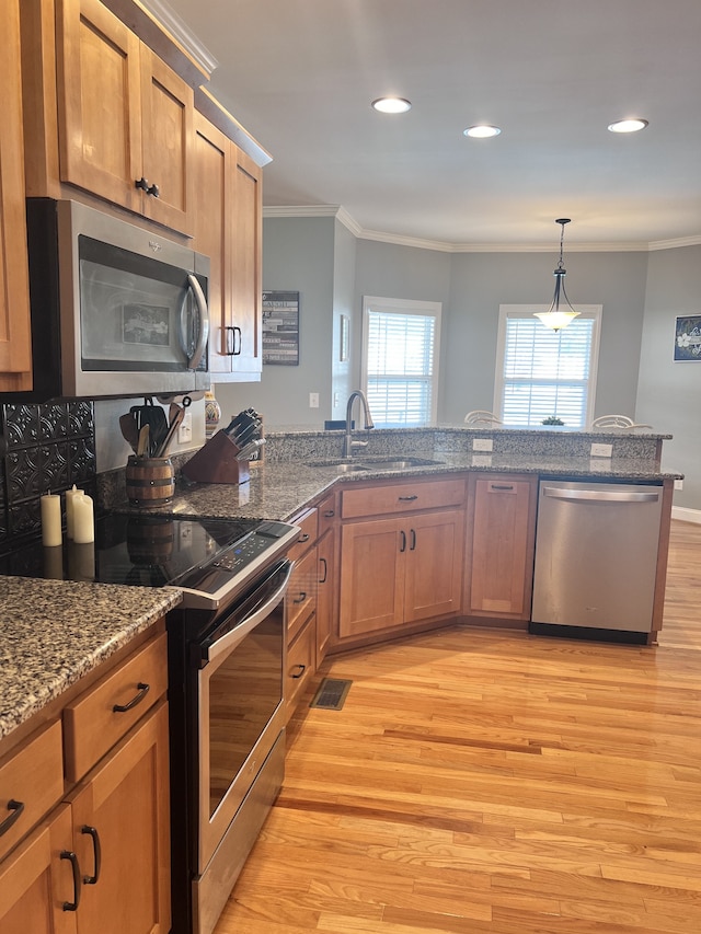 kitchen with sink, light wood-type flooring, ornamental molding, decorative light fixtures, and stainless steel appliances