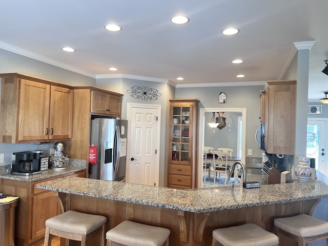 kitchen with crown molding, light stone countertops, a kitchen bar, kitchen peninsula, and stainless steel appliances