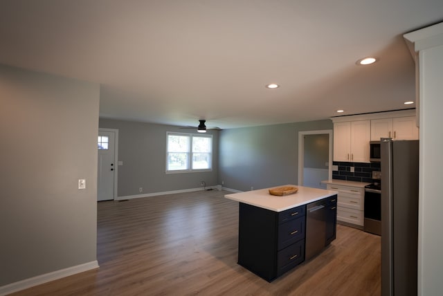 kitchen with ceiling fan, stainless steel appliances, a kitchen island, backsplash, and white cabinets