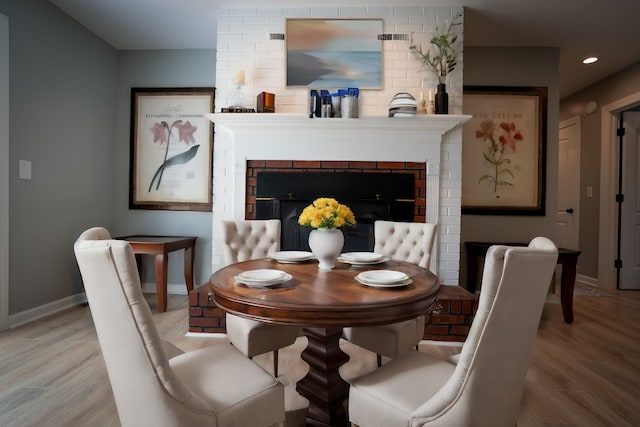 dining space featuring light hardwood / wood-style flooring and a brick fireplace