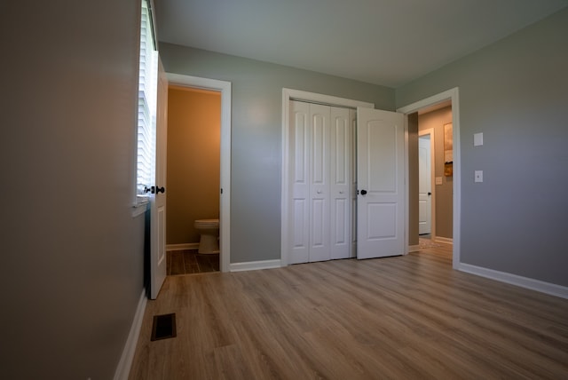 unfurnished bedroom featuring hardwood / wood-style floors, connected bathroom, and a closet