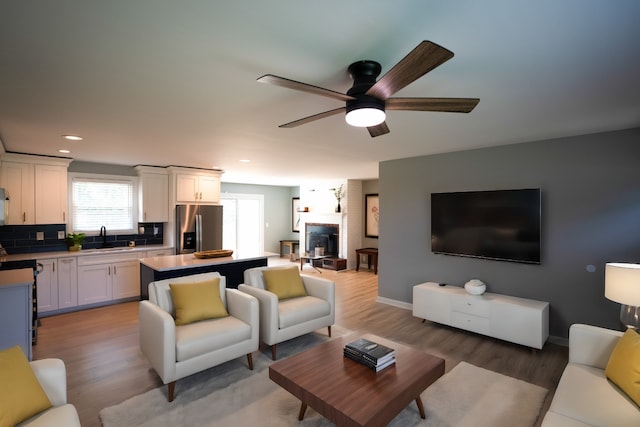 living room featuring hardwood / wood-style floors, a large fireplace, ceiling fan, and sink