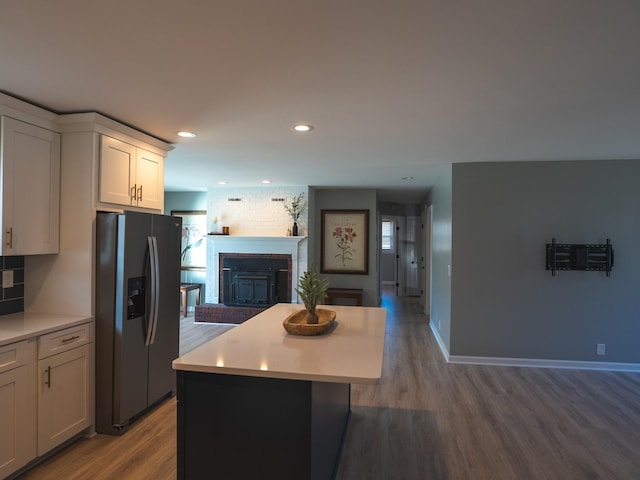 kitchen featuring a brick fireplace, white cabinetry, black refrigerator with ice dispenser, and hardwood / wood-style floors