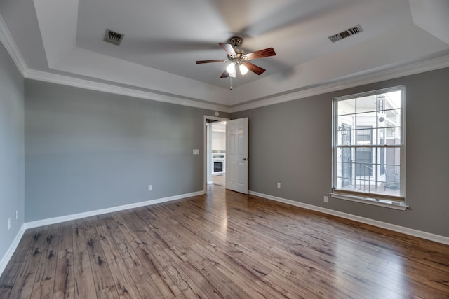 unfurnished room with wood-type flooring, a raised ceiling, and ornamental molding