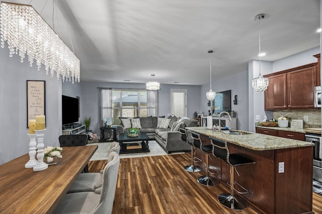 kitchen with dark wood-type flooring, sink, decorative backsplash, light stone counters, and a chandelier