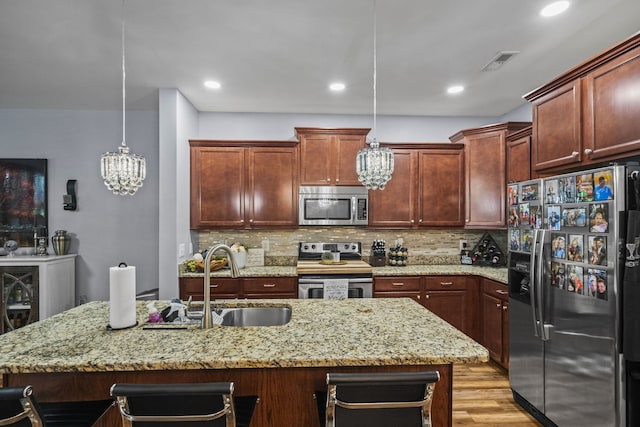 kitchen featuring sink, hanging light fixtures, tasteful backsplash, light hardwood / wood-style flooring, and appliances with stainless steel finishes