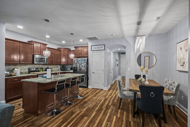 kitchen featuring light stone countertops, tasteful backsplash, stainless steel appliances, dark wood-type flooring, and hanging light fixtures