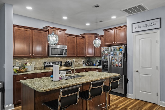 kitchen featuring light stone countertops, stainless steel appliances, hanging light fixtures, an island with sink, and decorative backsplash