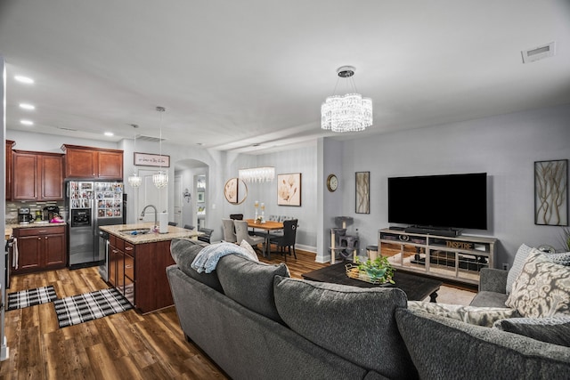 living room featuring sink, dark wood-type flooring, and an inviting chandelier