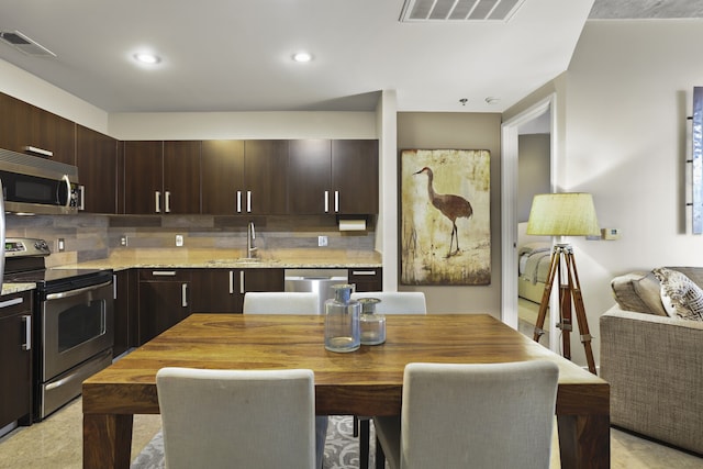 kitchen with backsplash, sink, appliances with stainless steel finishes, dark brown cabinets, and light stone counters