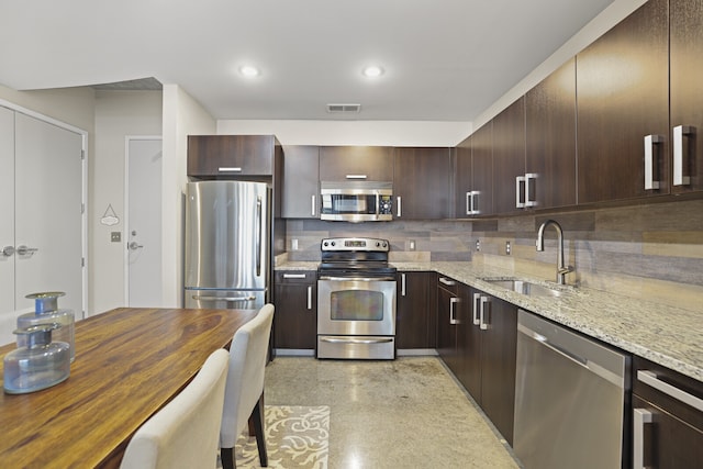 kitchen featuring backsplash, sink, light stone countertops, dark brown cabinets, and stainless steel appliances