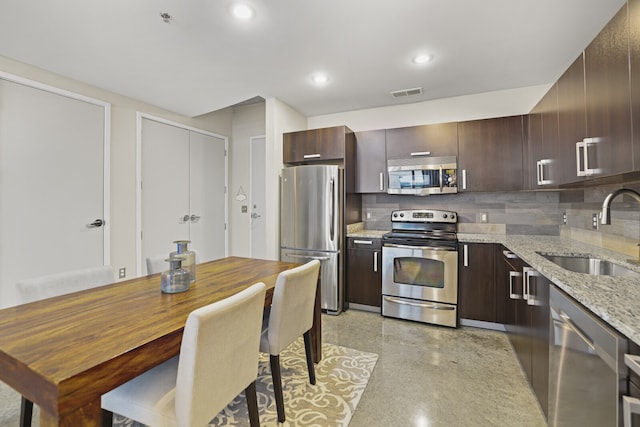 kitchen featuring appliances with stainless steel finishes, tasteful backsplash, light stone counters, dark brown cabinets, and sink