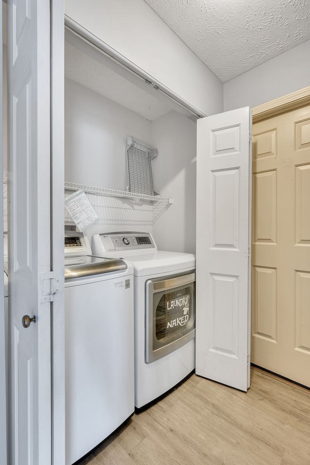 laundry area featuring washer and dryer, a textured ceiling, and light hardwood / wood-style flooring