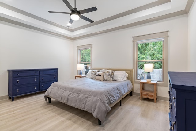 bedroom with light wood-type flooring, a tray ceiling, and ceiling fan