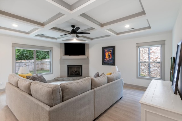 living room featuring a large fireplace, light hardwood / wood-style flooring, a healthy amount of sunlight, and coffered ceiling