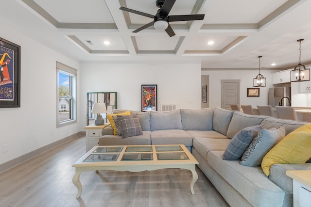 living room with beam ceiling, ceiling fan with notable chandelier, light hardwood / wood-style floors, and coffered ceiling