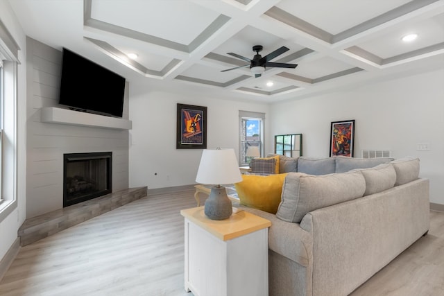 living room with light wood-type flooring, coffered ceiling, a large fireplace, ceiling fan, and beamed ceiling