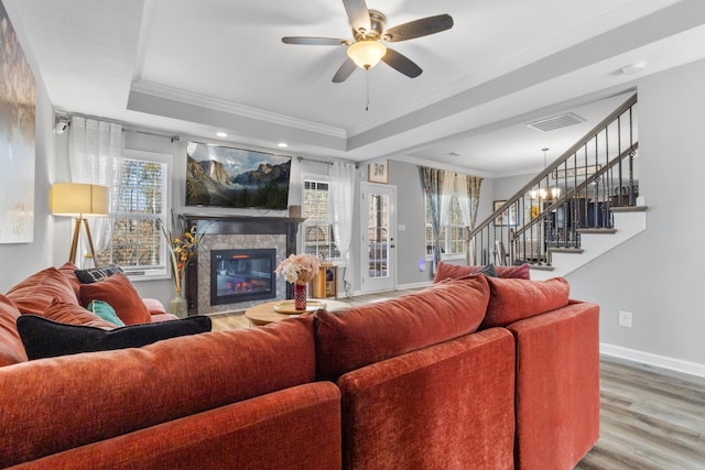 living room with wood-type flooring, ornamental molding, a raised ceiling, ceiling fan, and a fireplace