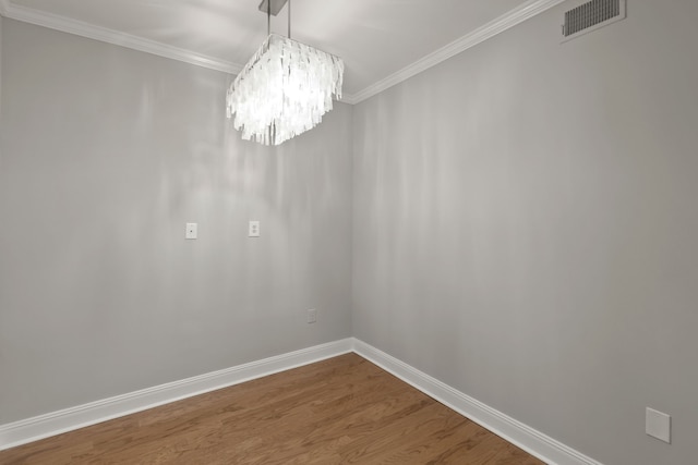 spare room with hardwood / wood-style floors, crown molding, and an inviting chandelier