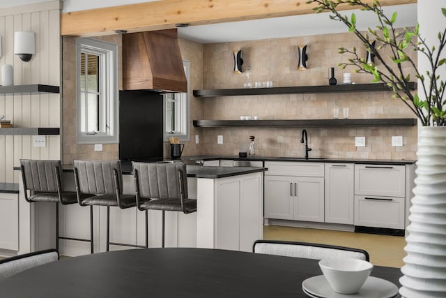 kitchen featuring sink, backsplash, white cabinetry, and custom exhaust hood