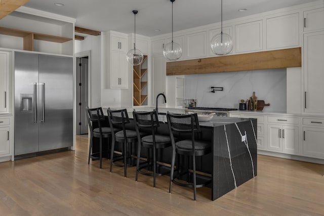 kitchen with white cabinets, appliances with stainless steel finishes, light hardwood / wood-style flooring, and an island with sink