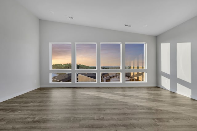 empty room with hardwood / wood-style flooring, vaulted ceiling, and a healthy amount of sunlight