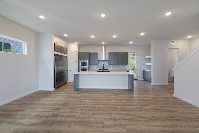 kitchen with sink, stainless steel appliances, an island with sink, gray cabinets, and light wood-type flooring