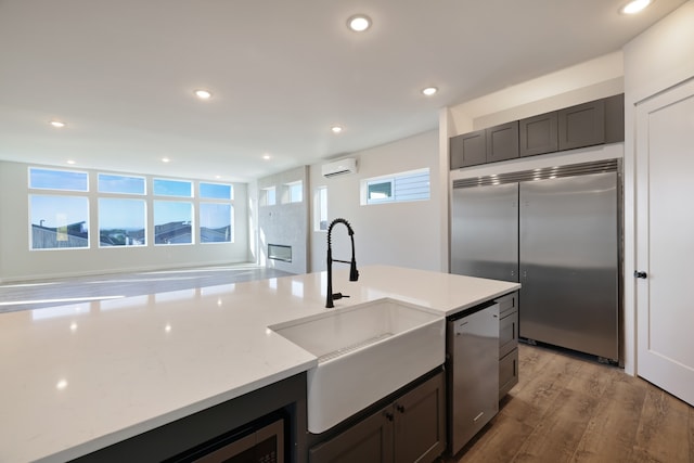 kitchen featuring appliances with stainless steel finishes, light wood-type flooring, light stone counters, a wall mounted AC, and sink