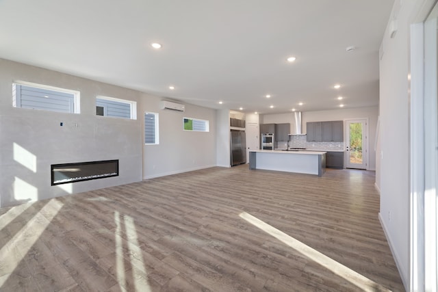 unfurnished living room with hardwood / wood-style flooring, a wall mounted air conditioner, and sink