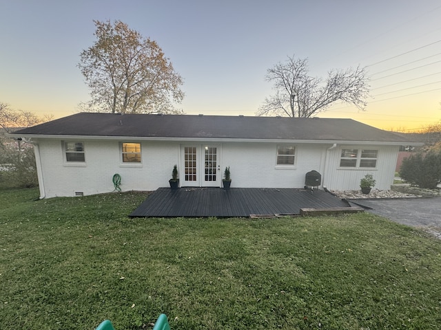 back house at dusk featuring a wooden deck and a yard