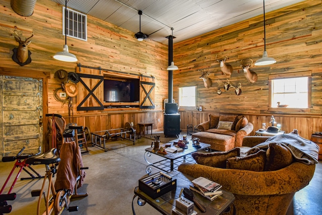 living room featuring wood walls, a barn door, concrete flooring, and a towering ceiling