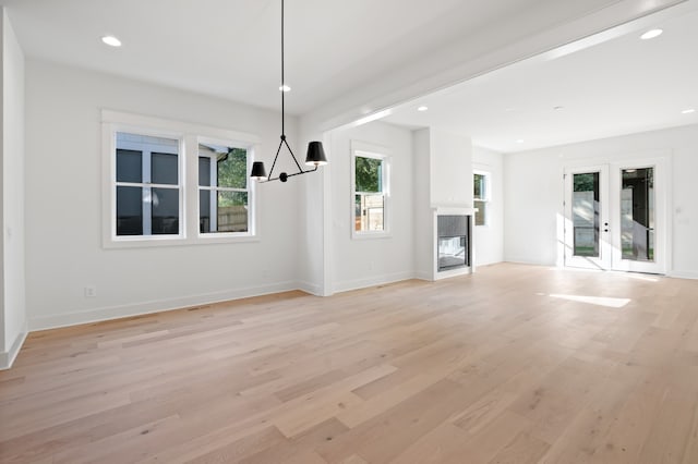 unfurnished living room with light wood-type flooring, french doors, and a chandelier