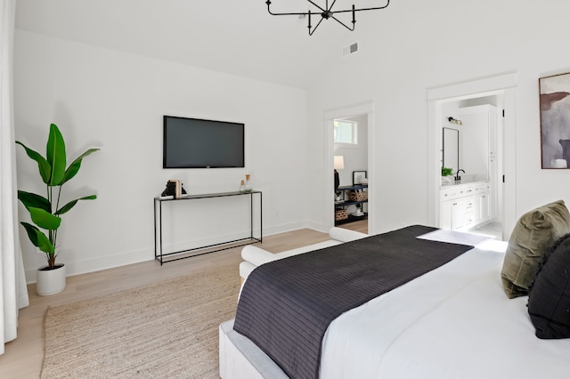 bedroom with ensuite bath, light hardwood / wood-style flooring, and a chandelier