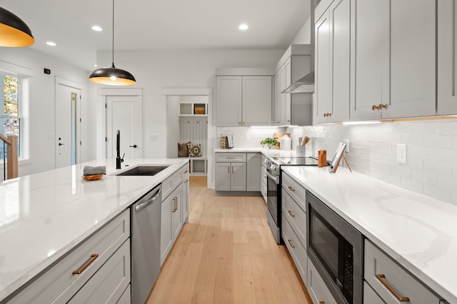 kitchen with appliances with stainless steel finishes, light wood-type flooring, sink, gray cabinets, and hanging light fixtures