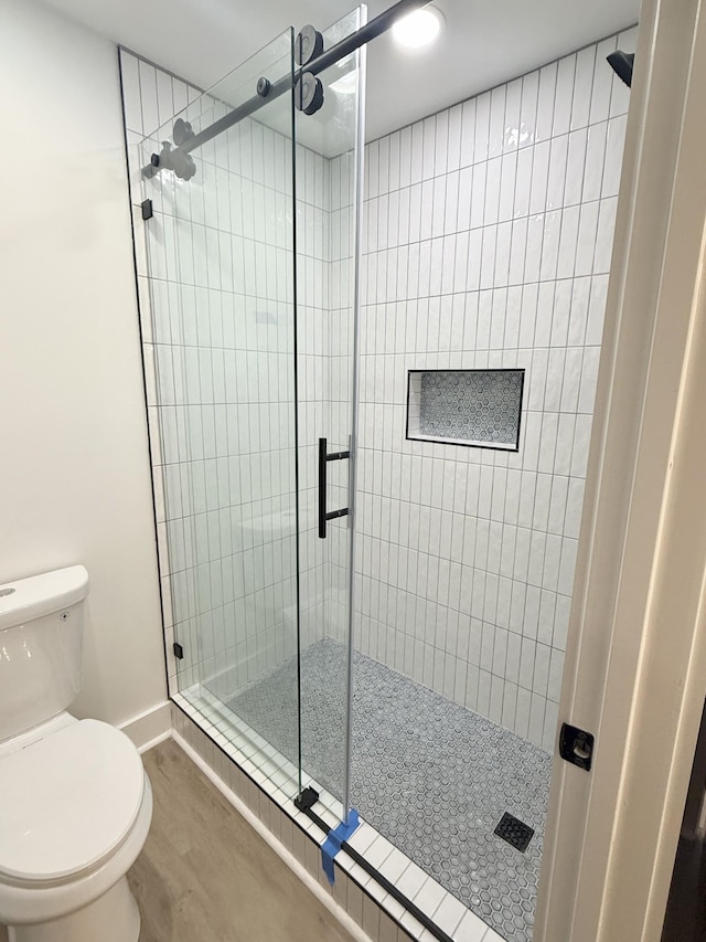 bathroom featuring toilet, a shower with door, and wood-type flooring