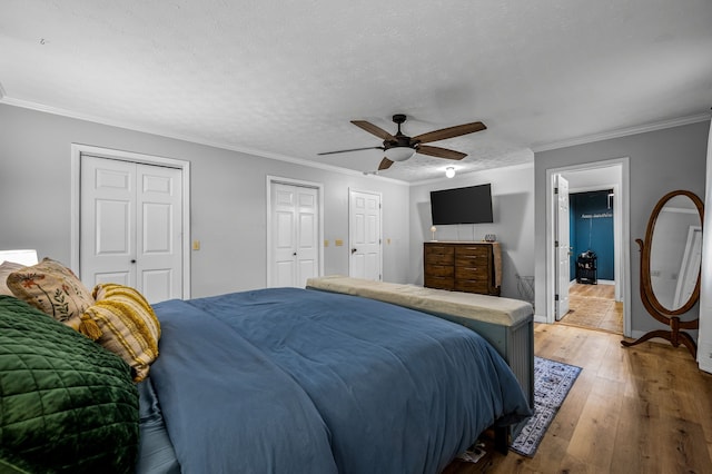 bedroom featuring hardwood / wood-style flooring, ornamental molding, two closets, and a textured ceiling