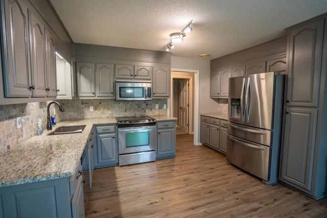 kitchen with decorative backsplash, a textured ceiling, stainless steel appliances, sink, and light hardwood / wood-style floors