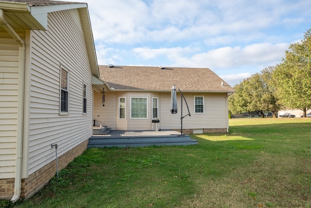 rear view of property featuring crawl space, a deck, a lawn, and roof with shingles