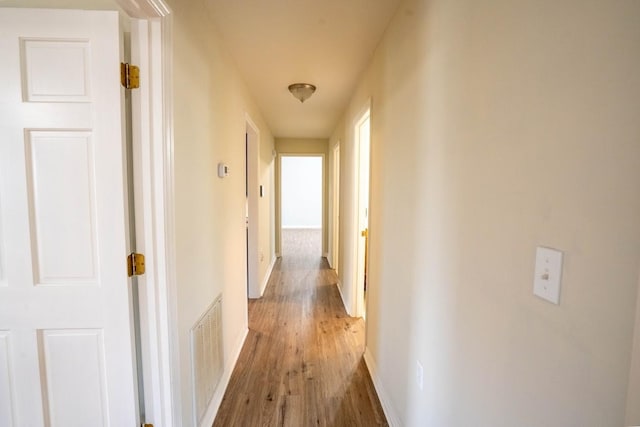 hallway with light wood-style floors, baseboards, and visible vents