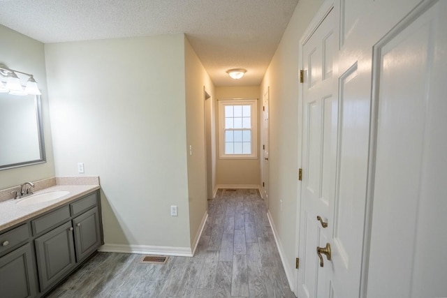 bathroom with a textured ceiling, baseboards, wood finished floors, and vanity