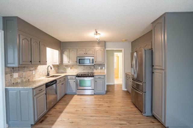 kitchen with decorative backsplash, gray cabinetry, appliances with stainless steel finishes, a sink, and light wood-type flooring