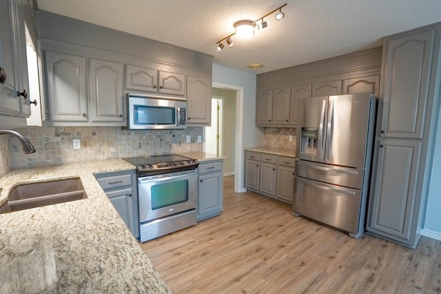 kitchen featuring light wood-style flooring, light stone countertops, a sink, appliances with stainless steel finishes, and decorative backsplash