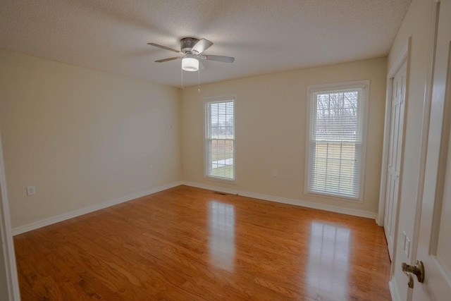 empty room featuring light wood-type flooring, baseboards, and a textured ceiling