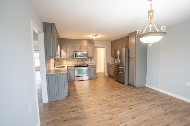 kitchen with stainless steel appliances, tasteful backsplash, gray cabinetry, a sink, and light wood-type flooring