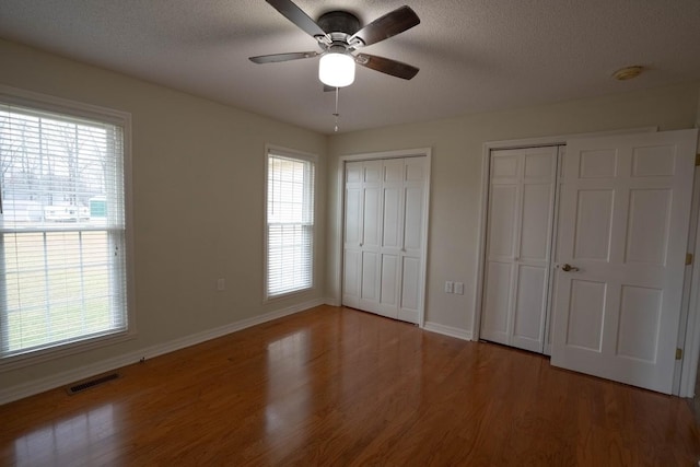 unfurnished bedroom with visible vents, multiple windows, light wood-style flooring, and two closets