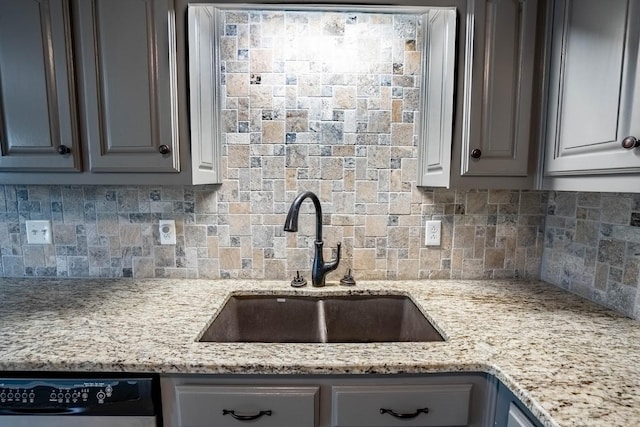 kitchen with tasteful backsplash, dishwasher, light stone countertops, gray cabinetry, and a sink